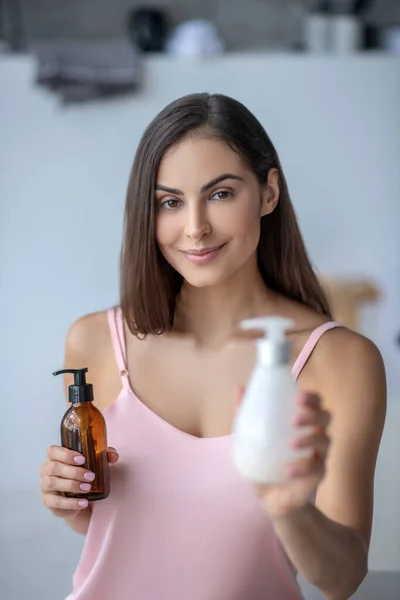 Mujer de pelo bastante largo sosteniendo botellas con loción corporal — Foto de Stock