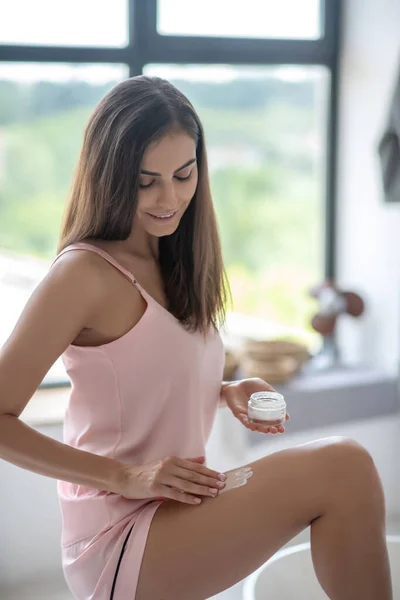 Mujer de pelo bastante largo aplicando loción corporal en su pierna — Foto de Stock