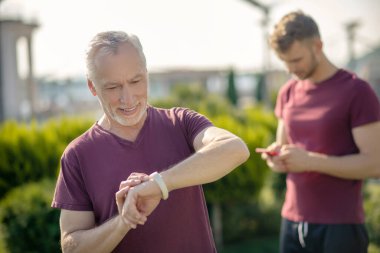 Olgun adam akıllı adam, genç erkek arkasında akıllı telefonu kontrol ediyor.