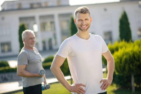 Bearded male smiling, hands on hips, grey-haired man holding dumbbells behind — Stock Photo, Image