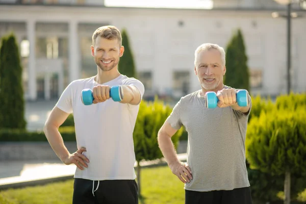 Ung man och gråhårig man med hantel i ena handen, en annan hand på höften — Stockfoto