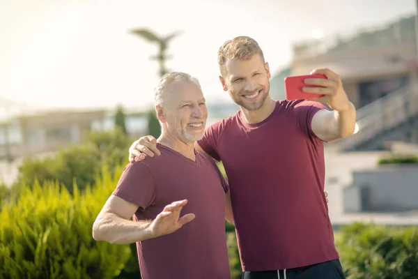 Бородатый мужчина и зрелый мужчина делает селфи во время тренировки, улыбаясь — стоковое фото
