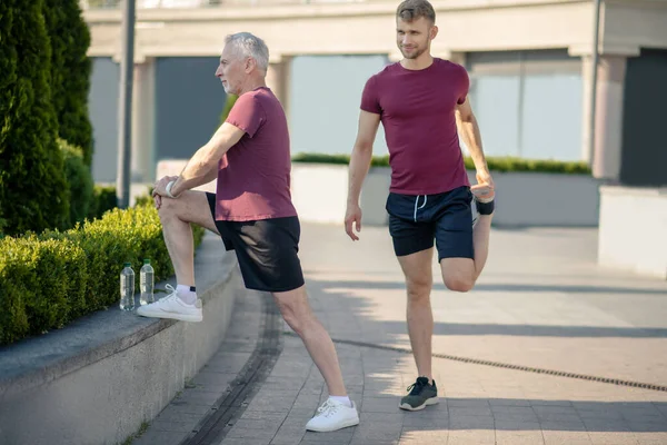 Gri saçlı, dizini uzatan, yanında uzanan genç bir erkek. — Stok fotoğraf