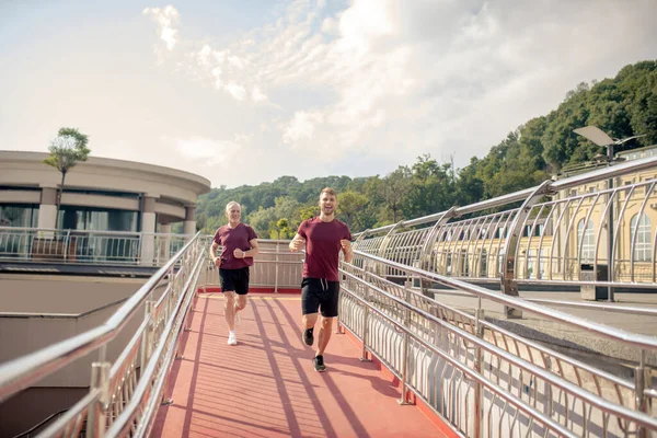 Genç erkek ve gri saçlı adam köprüde koşuyor, gülümsüyor. — Stok fotoğraf