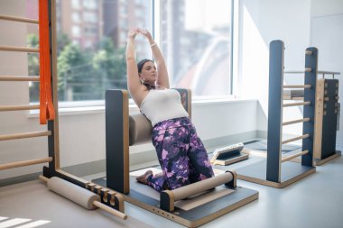 Koyu saçlı, iri yarı, arkaya yaslanan ve esneyen bir kadın.