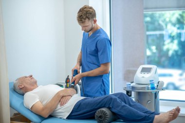 Sakallı doktor olgun hastaya ultrason dirsek tedavisi uyguluyor.