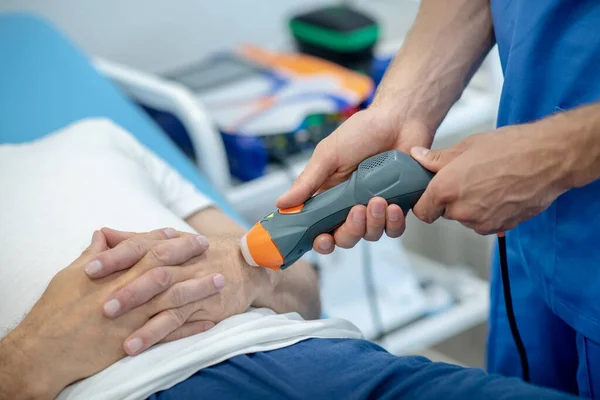 Крупним планом чоловічий пацієнт лежить на тренері, отримуючи ультразвукове лікування руки — стокове фото