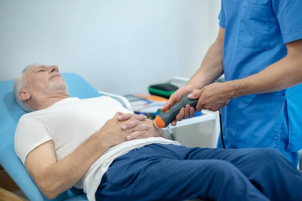 Paciente masculino de pelo gris acostado en el entrenador, recibiendo tratamiento con ultrasonido de la mano —  Fotos de Stock