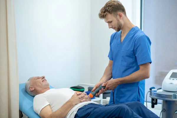 Γενειοφόρος φυσιοθεραπευτής εκτελεί υπερηχογράφημα χέρι θεραπεία σε ώριμο ασθενή — Φωτογραφία Αρχείου
