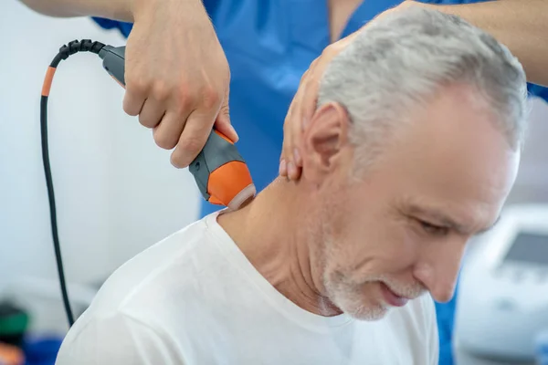 Paciente masculino de pelo gris que recibe tratamiento de ultrasonido en el cuello, doblando la cabeza —  Fotos de Stock