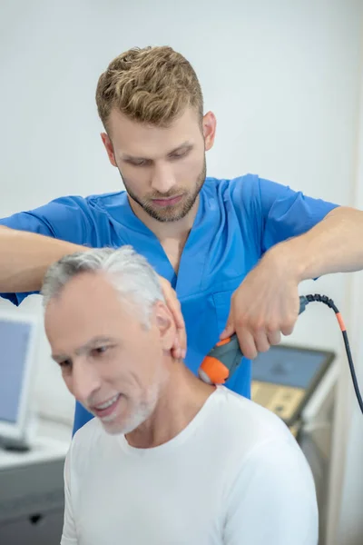 Бородатий лікар, який проводить лікування ультразвукової шиї на усміхненого зрілого пацієнта — стокове фото