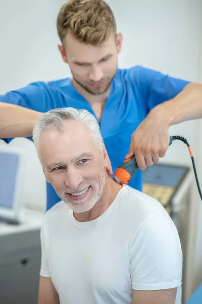 Vousatý lékař provádějící ultrazvukové ošetření krku u usmívajícího se muže — Stock fotografie