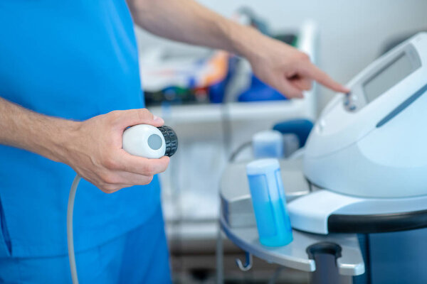 Close-up of male hands pressing buttons on physiotherapy ultrasound machine