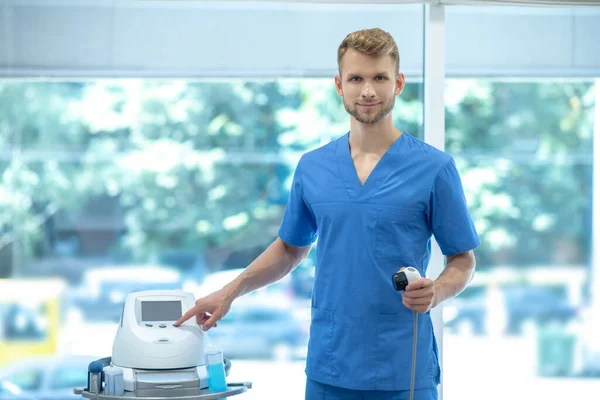 Médico joven barbudo ajustando los ajustes en la máquina de ultrasonido de fisioterapia — Foto de Stock