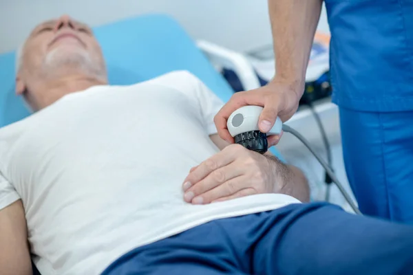 Grauhaarige männliche Patientin liegt auf Reisebus und erhält Ultraschall-Handbehandlung — Stockfoto