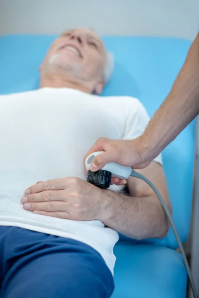 Paziente maschio dai capelli grigi sdraiato sul pullman, sottoposto a trattamento ecografico alle mani — Foto Stock