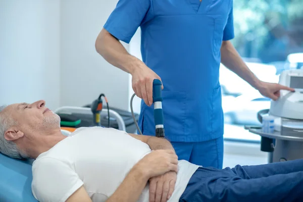 Grauhaarige männliche Patientin liegt auf Reisebus und erhält Ultraschall-Ellbogenbehandlung — Stockfoto