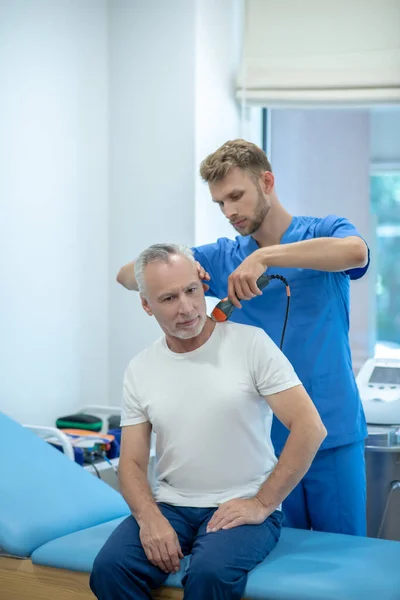 Бородатый врач, проводящий ультразвуковое лечение шеи у взрослого пациента — стоковое фото