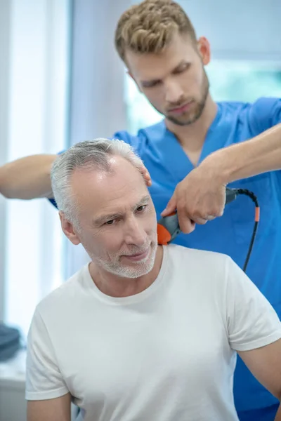 Bearded doctor performing ultrasound neck treatment on mature patient — Stock Photo, Image