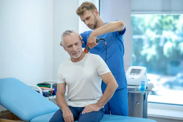 Mature patient sitting on coach, receiving ultrasound treatment of his neck — Stock Photo, Image