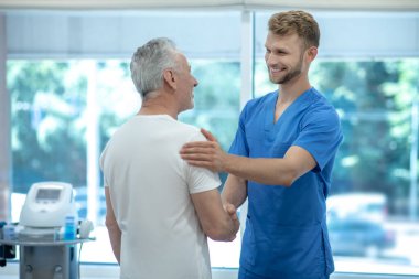 Genç doktor yaşlı bir hastaya el sıkışıyor.