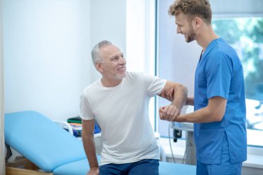 Genç doktor hastanın koltuğa oturmasına yardım ediyor.
