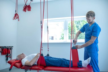 Kanepede yatan yaşlı bir adam ve rehabilitasyon uzmanı.