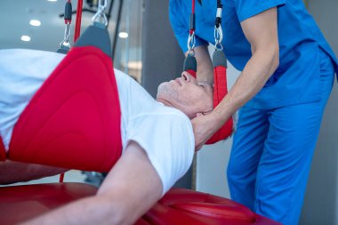 Mavi elbiseli doktor yaşlı adamların boynuna masaj yapıyor.