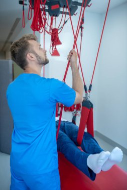 Doktor asılan kayışları elleriyle çekiyor.