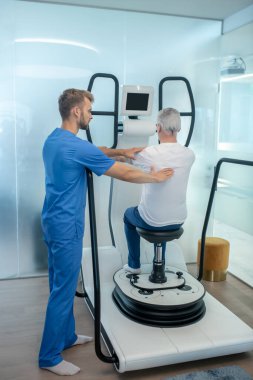 Hasta simülatörde oturuyor ve rehabilitasyon terapistini destekliyor.