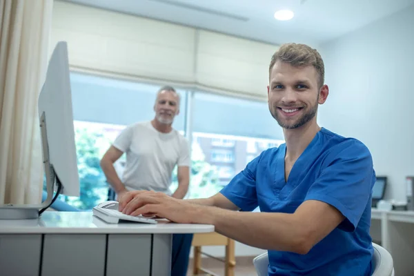 Jovem médico sorridente e paciente idoso no consultório — Fotografia de Stock