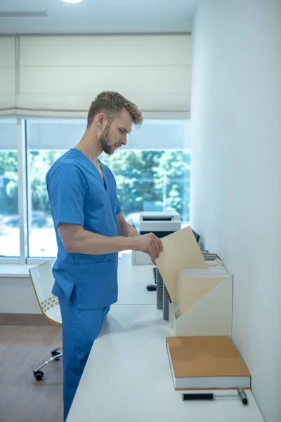 Bärtiger junger Arzt legt Papiere in stehenden Aktenordner — Stockfoto