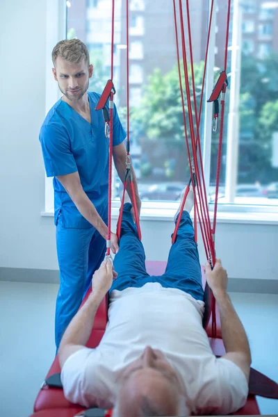 Hombre terapeuta de rehabilitación ayudando a elevar las piernas de los pacientes — Foto de Stock