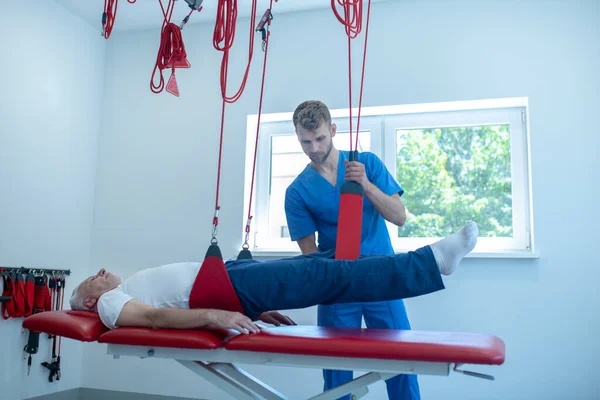 Седовласый мужчина лежит на диване во время процедур и доктор — стоковое фото