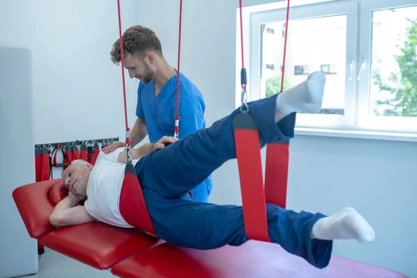 Ejercicio del anciano con un joven capacitador rehabilitador — Foto de Stock