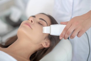 Koyu renk saçlı kadın güzellik salonunda güzellik tedavisi görüyor ve kendini rahat hissediyor.