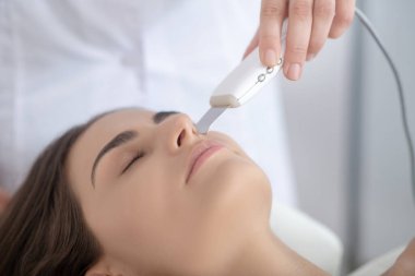 Siyah saçlı kadın lazer tedavisi görüyor ve rahatlamış görünüyor.