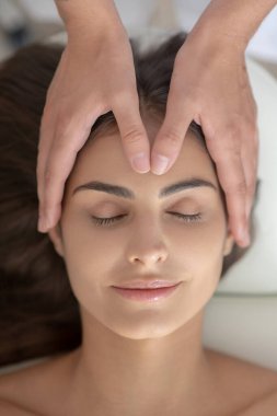 Masaj terapisti bir kadının alnına masaj yapıyor.