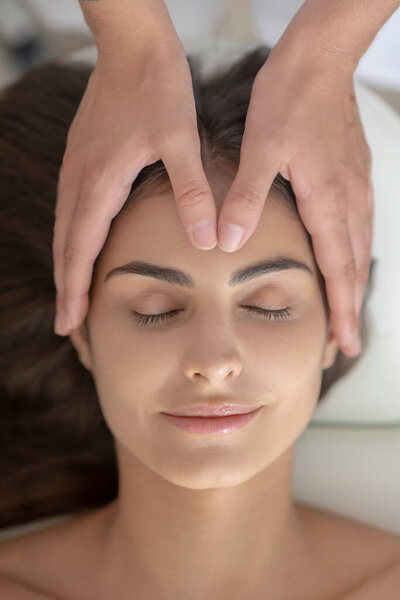 Массажист массирует лоб женщины