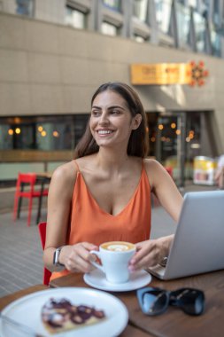 Kahve içen ve gülümseyen modaya uygun genç bir kadın.