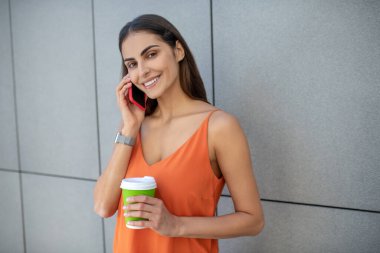 Elinde akıllı bir telefon ve bir fincan kahve tutan güzel bir kadın.