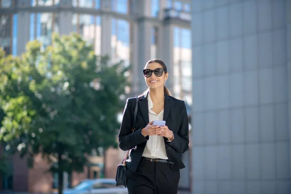 Elegante mujer morena en gafas de sol caminando por la calle — Foto de Stock