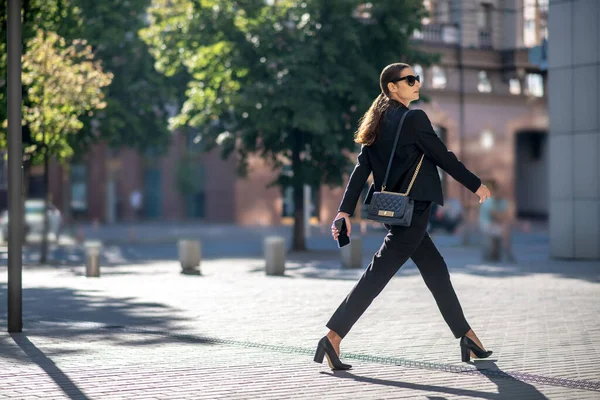 Elegant mörkhårig kvinna i solglasögon korsar gatan — Stockfoto
