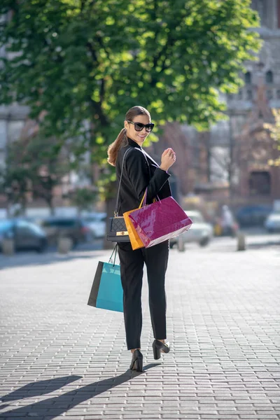Wysoka ciemnowłosa kobieta z torbami na zakupy chodząca ulicą — Zdjęcie stockowe