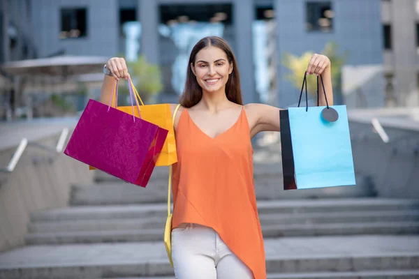Leende kvinna i orange skjorta visar shoppingväska — Stockfoto