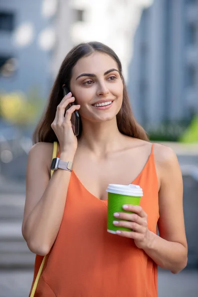 Mujer sonriente sosteniendo una taza de café y hablando por teléfono — Foto de Stock