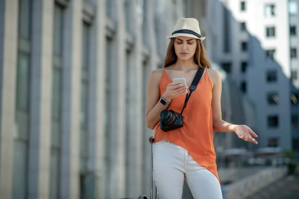 Mörkhårig ung kvinna i en hatt innehav smartphone och ser störd — Stockfoto