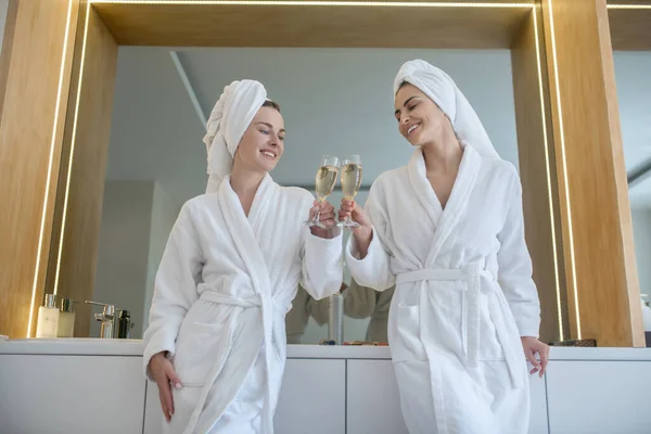 Zwei hübsche Mädchen in weißen Roben verbringen Zeit miteinander und trinken Champagner — Stockfoto