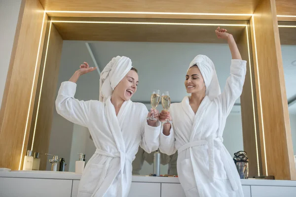 Dos chicas guapas con túnicas blancas pasando tiempo juntas y festejando — Foto de Stock