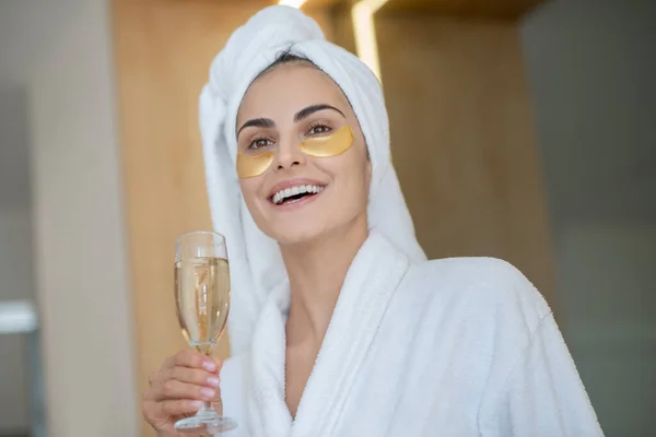 Söt leende flicka med ögonlappar och glas champagne — Stockfoto